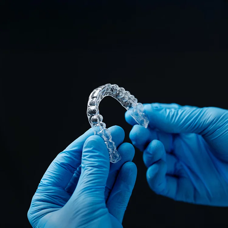 A clear aligner tray held up in gloved hands