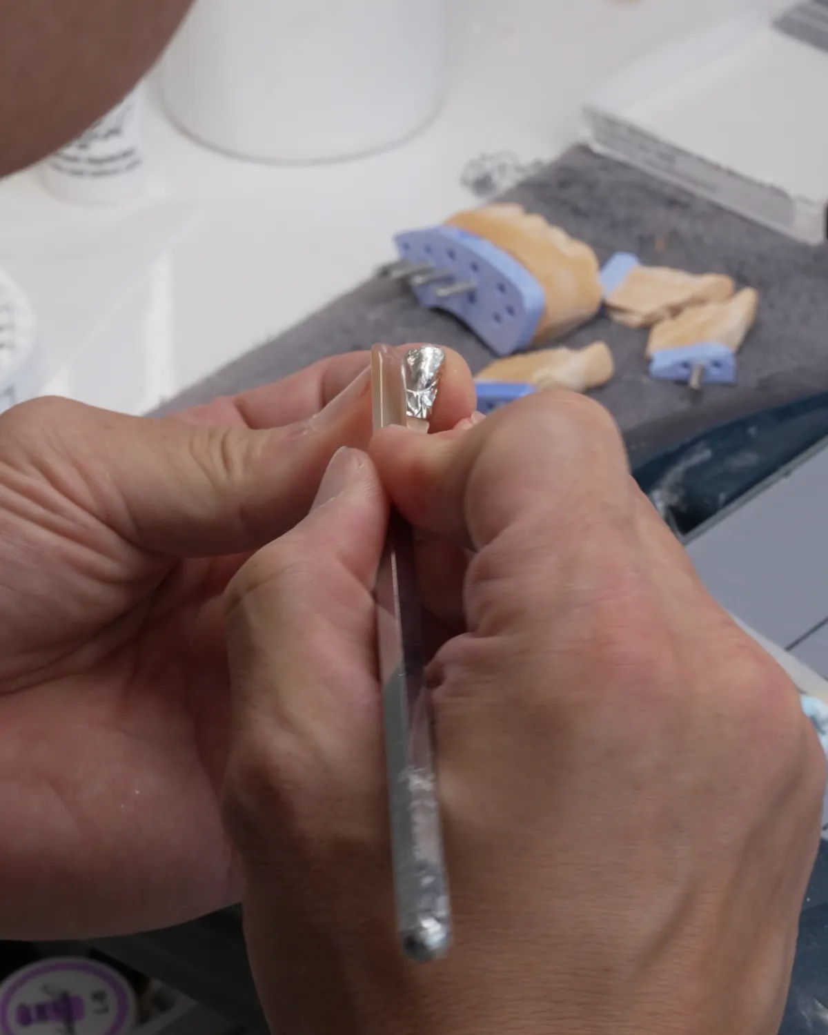 A master&rsquo;s hands holding a die and a fine brush at the bench