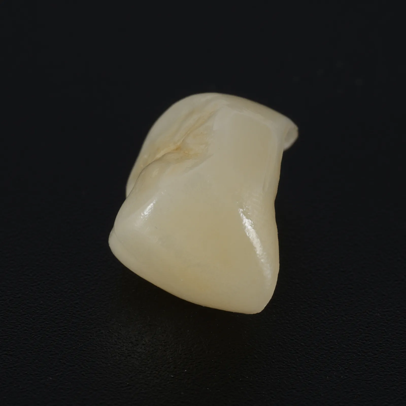 A monolithic zirconia crown, stained and glazed, standing on a black glossy ground