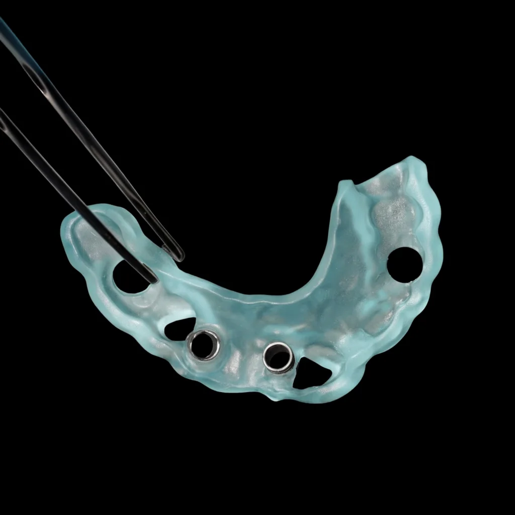 A surgical guide with its metal sleeves, held in tweezers on a black ground