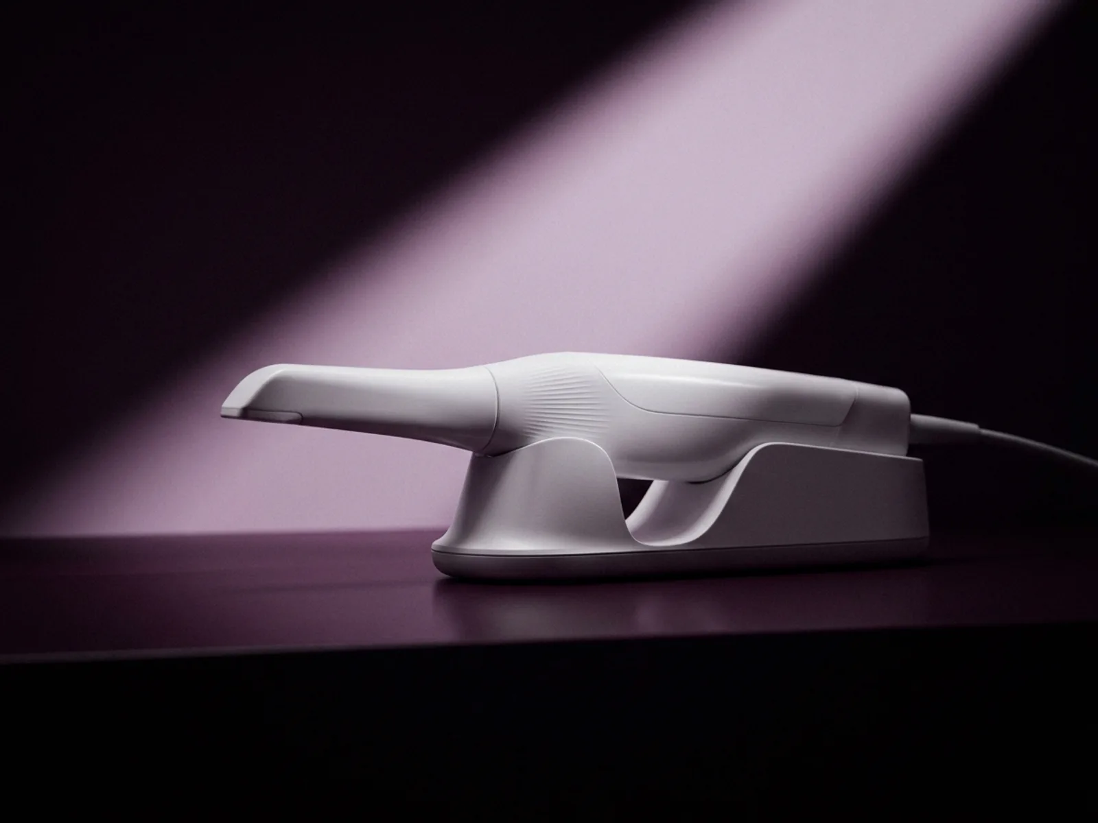 An intraoral scanner wand resting on its cradle under a single beam